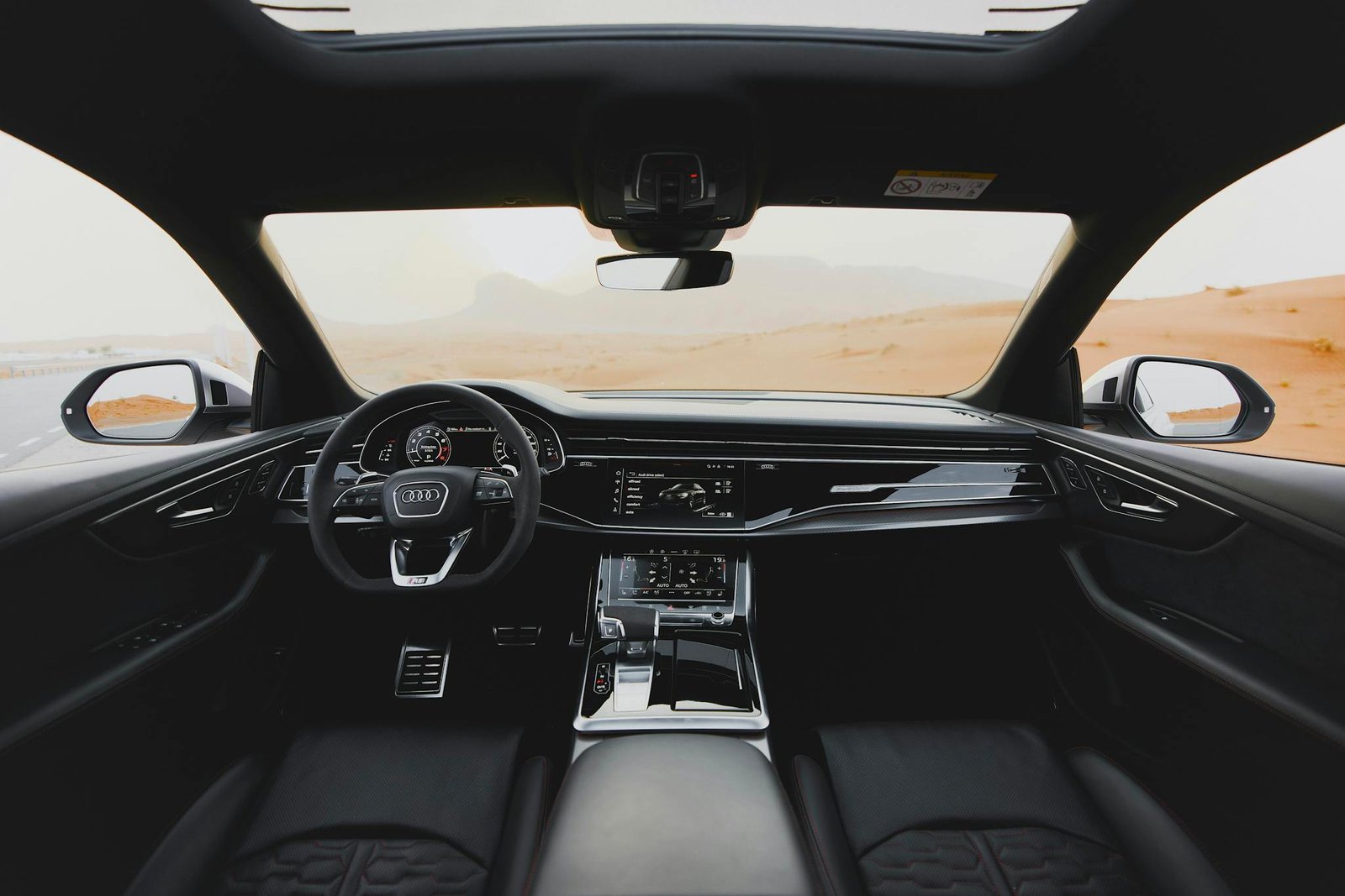 A sleek luxury car interior with a panoramic view of a desert landscape.